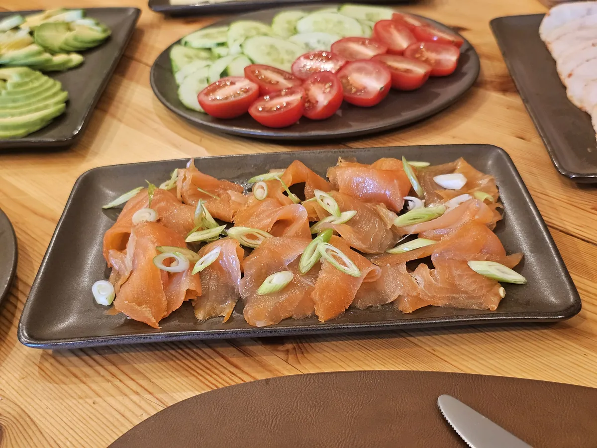 A platter of smoked salmon with spring onion, tomatoes and cucumber