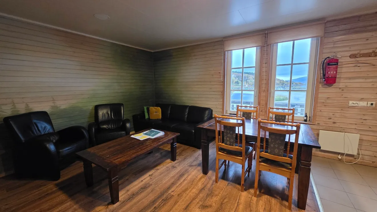Living room with armchairs, dining table and sea-view windows in the Skog apartment at Troll Havn, Vikran